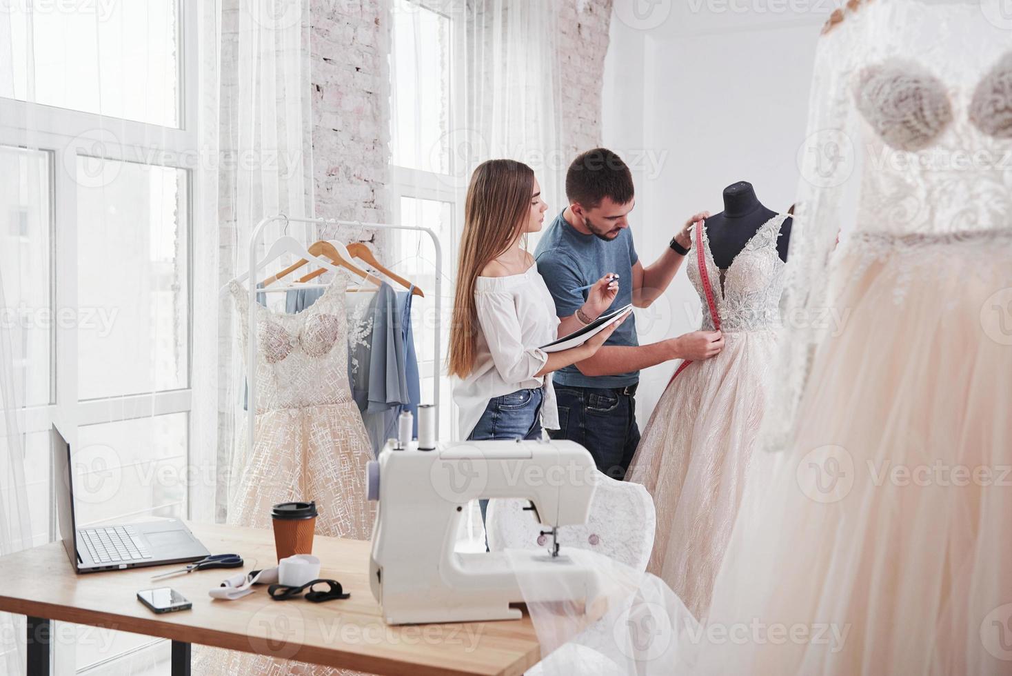 deux personnes mesurent la place du tissu sur la poitrine. le processus d'essayage de la robe dans l'atelier de vêtements fabriqués à la main photo