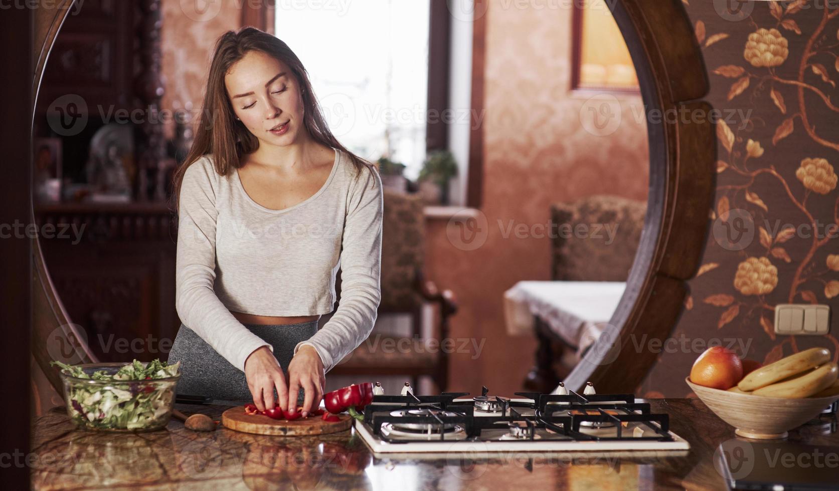 faire sa salade préférée. jolie jeune femme debout dans la cuisine moderne près de la cuisinière à gaz et préparant la nourriture photo