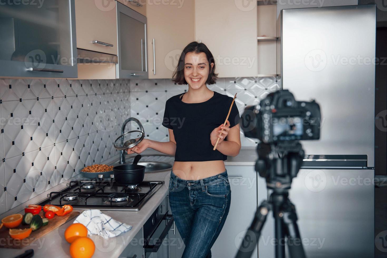 veuillez sourire à la caméra qui se tient devant vous. fille dans la cuisine moderne à la maison le week-end du matin photo