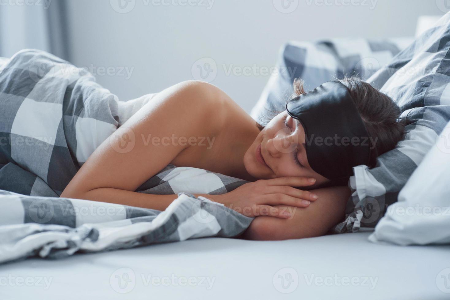 une femme avec un masque aux yeux bandés pour dormir est allongée sur le lit le matin photo