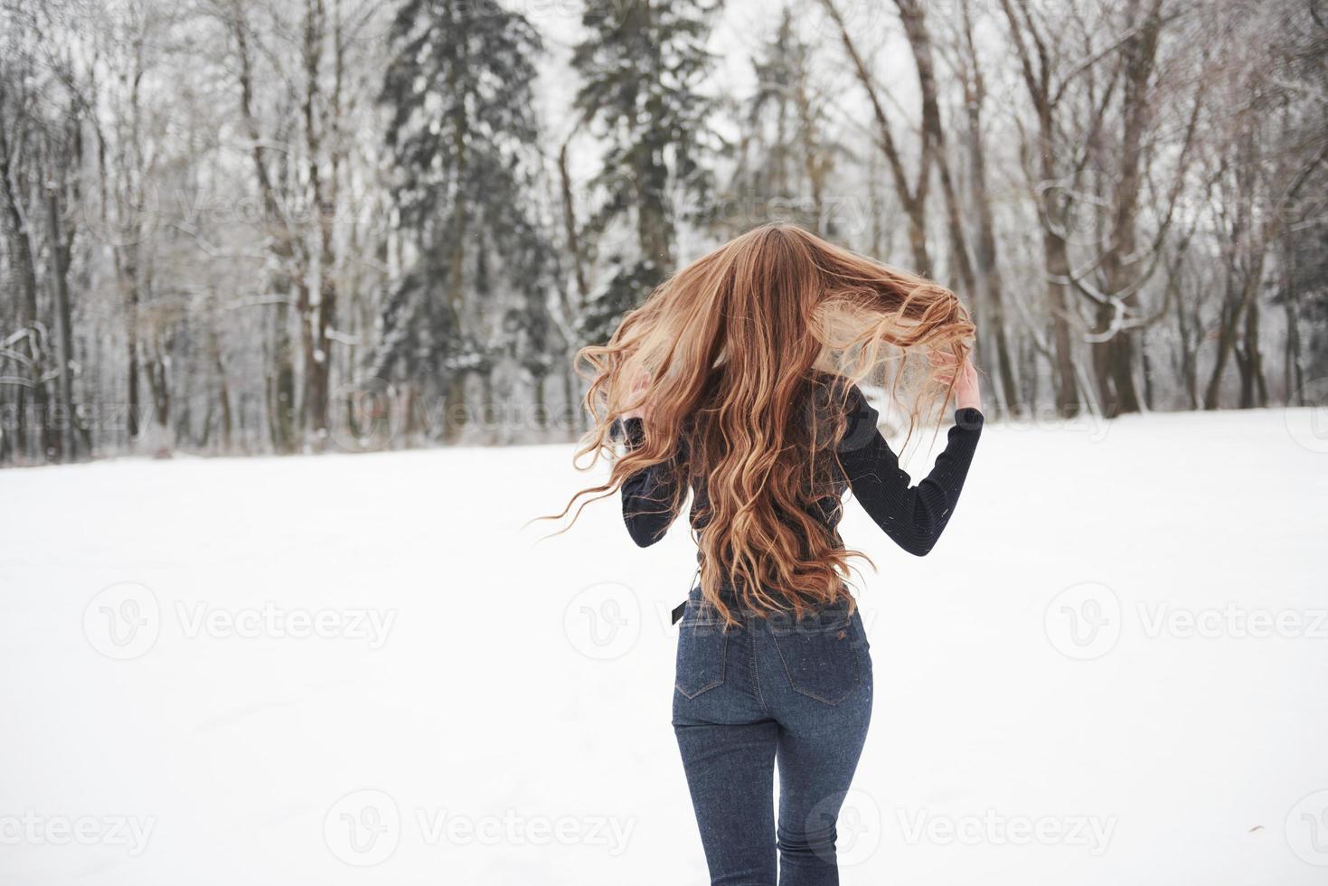 cheveux sur les différents côtés. vue arrière d'une fille aux cheveux longs court près de la forêt jusqu'à l'automobile en hiver photo