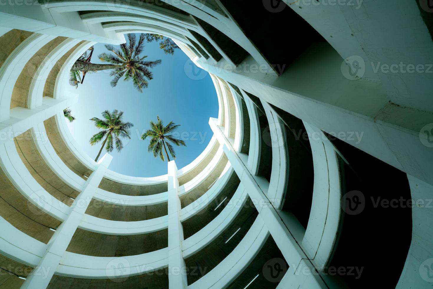 vue de dessous bâtiment de parking à plusieurs étages avec cocotier au-dessus du bâtiment en été. garage de stationnement à plusieurs niveaux. parking intérieur. architecture du bâtiment à courbe en spirale. construction durable. photo