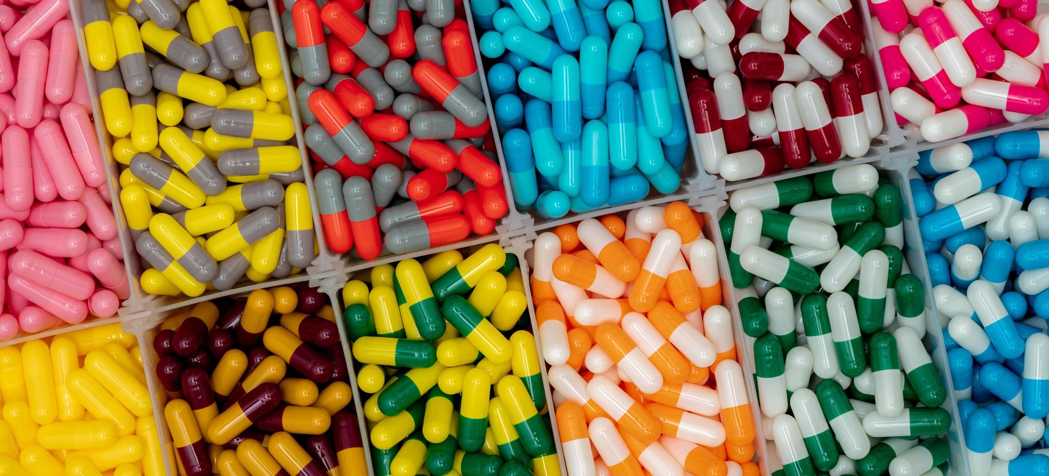 pilules de capsule colorées dans une boîte en plastique. industrie pharmaceutique. capsules roses, jaunes, bleues, vertes, orange, grises, rouges et blanches. la santé et la médecine. concept de vitamines et de suppléments. photo