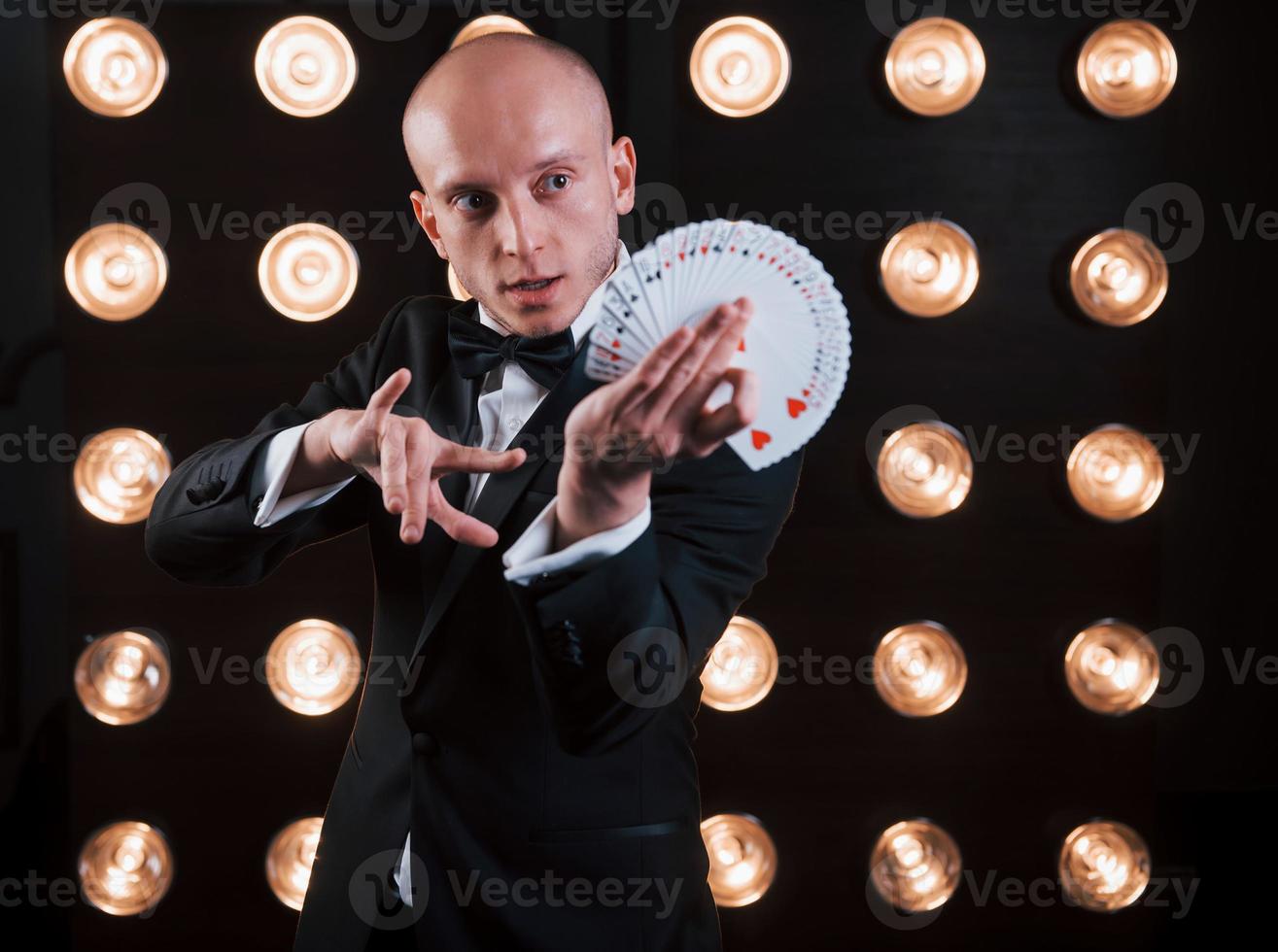 dextérité des mains. magicien en costume noir et avec des cartes à jouer debout dans la pièce avec un éclairage spécial dans les coulisses photo