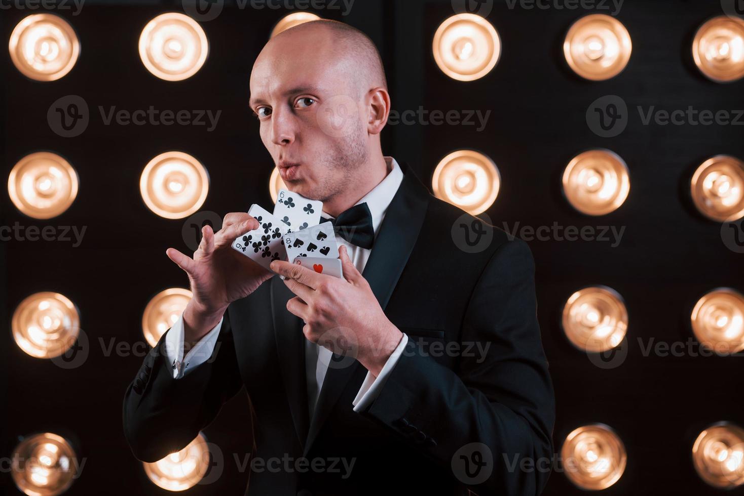 ça va t'impressionner. magicien en costume noir et avec des cartes à jouer debout dans la pièce avec un éclairage spécial dans les coulisses photo