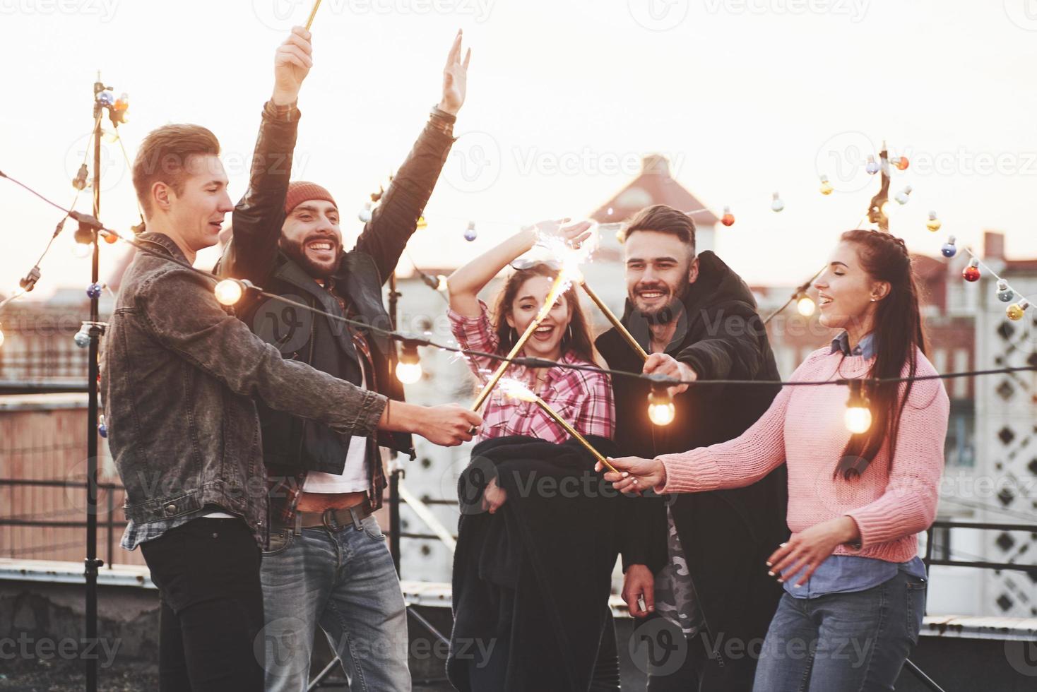 fête les vacances. jouer avec des cierges magiques sur le toit. groupe de jeunes beaux amis photo