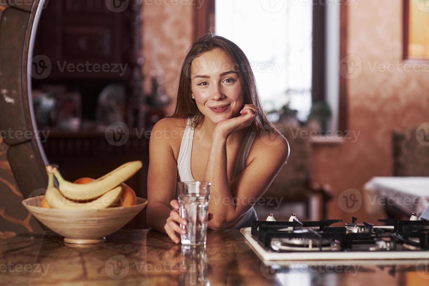 tenant un verre avec de l'eau. jeune femme debout dans la cuisine moderne près de la cuisinière à gaz photo