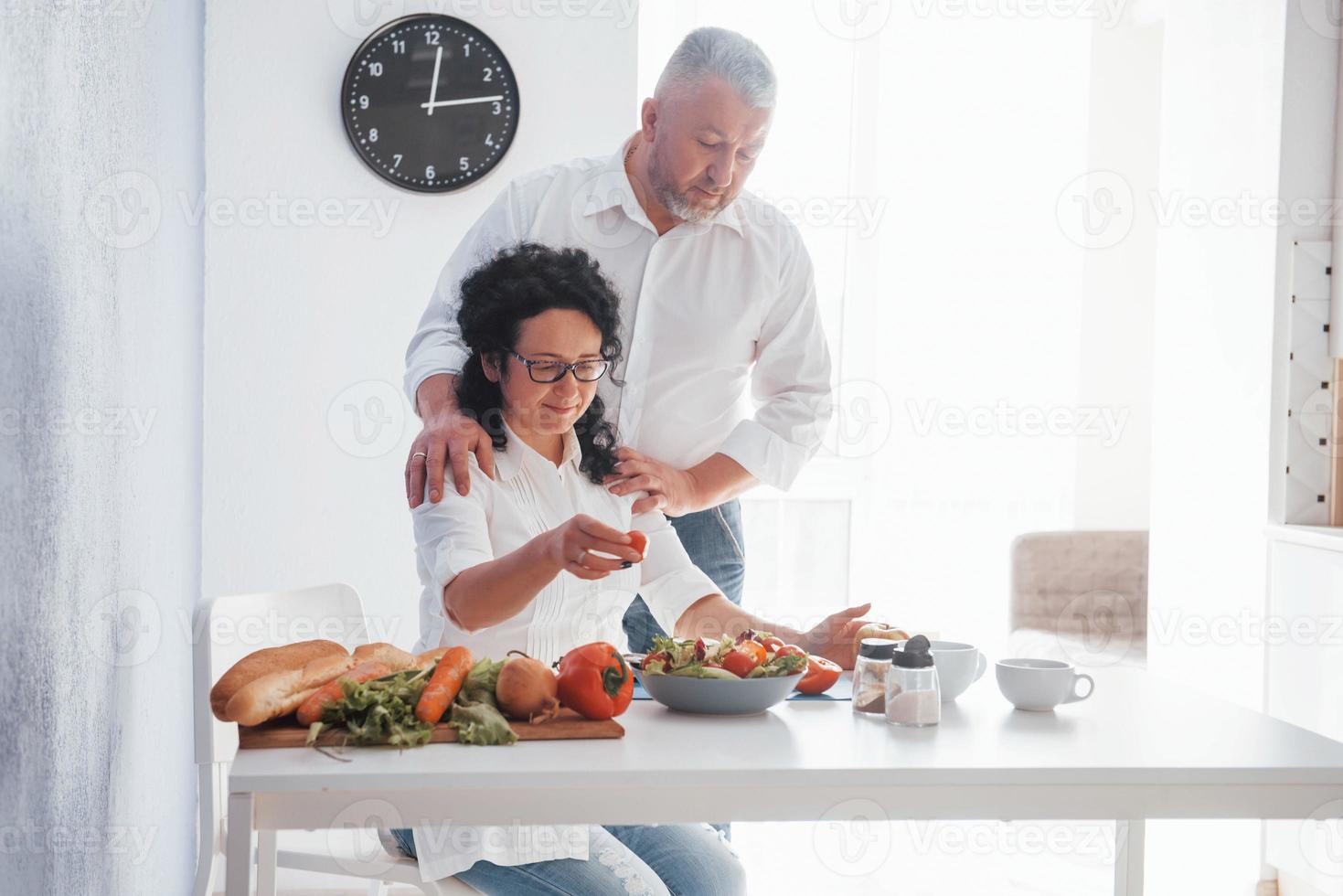 mangeons ça. homme et sa femme en chemise blanche préparant de la nourriture dans la cuisine à l'aide de légumes photo