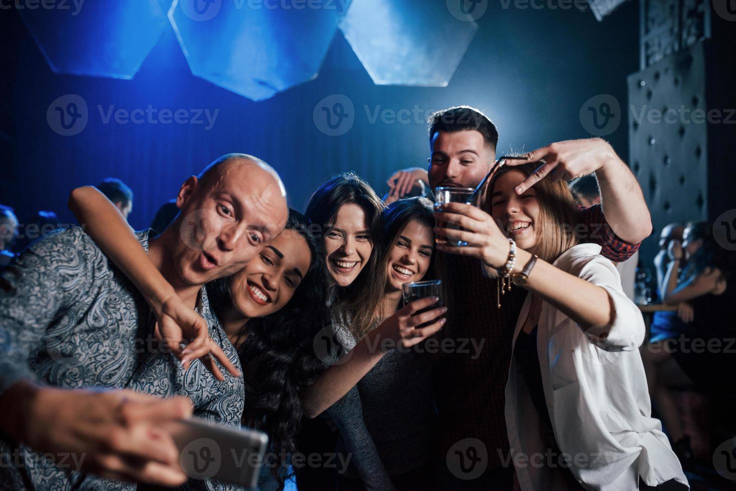 faire une drôle de tête. amis prenant selfie dans une belle discothèque. avec des boissons dans les mains photo