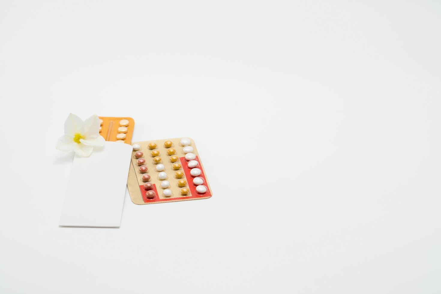 pilules contraceptives ou pilule contraceptive avec étui en papier et fleur blanche sur fond blanc. concept de planification familiale. la thérapie de remplacement d'hormone. traitement hormonal de l'acné avec pilule anti-androgène. photo