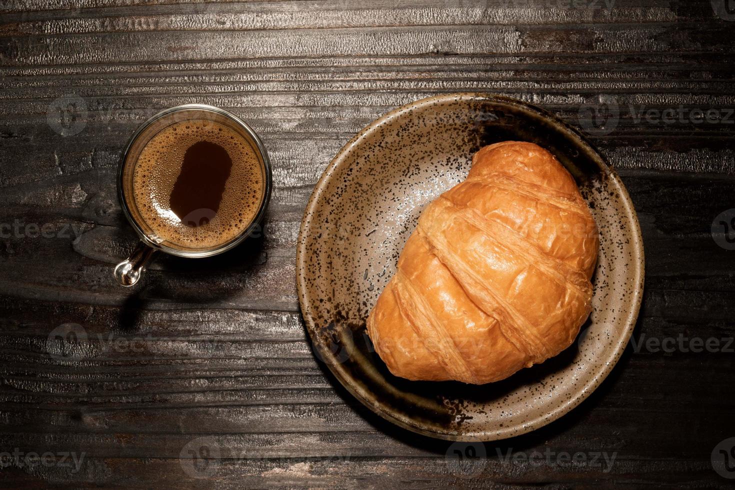 petit-déjeuner croissant dans l'assiette et café sur table en bois. photo