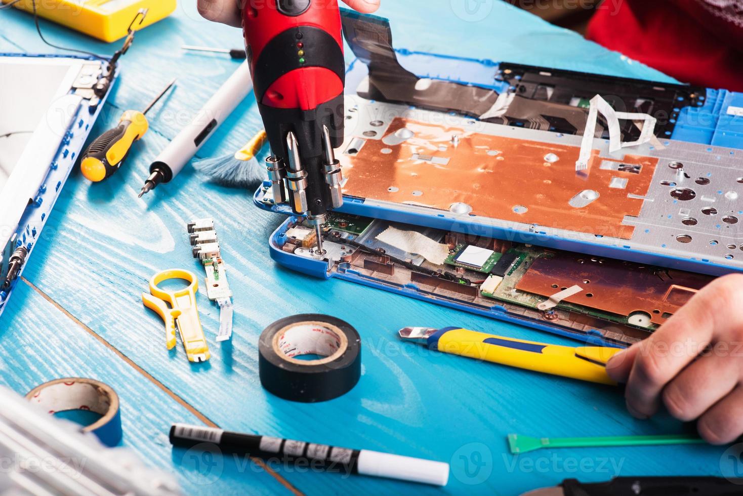 l'assistant répare l'ordinateur portable avec des outils et des mains sur la table en bois bleue. vue de dessus photo