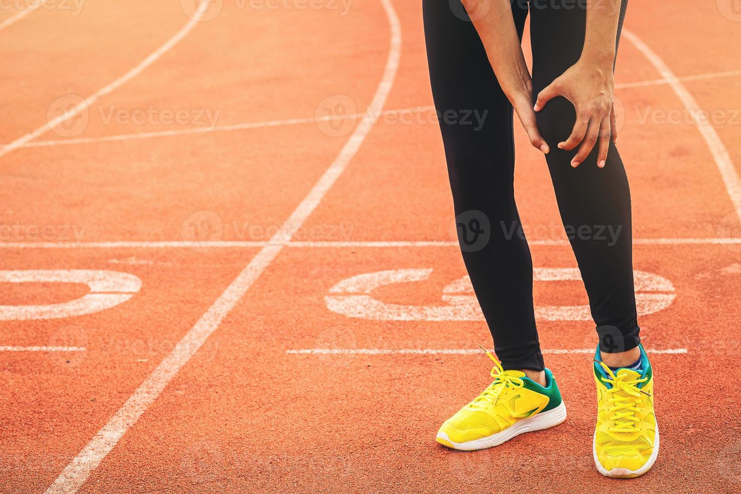 femme de coureur avec une blessure au genou en cours d'exécution sportive à l'hippodrome. mains tenant le genou avec une torsion douloureuse du genou à la cheville. photo