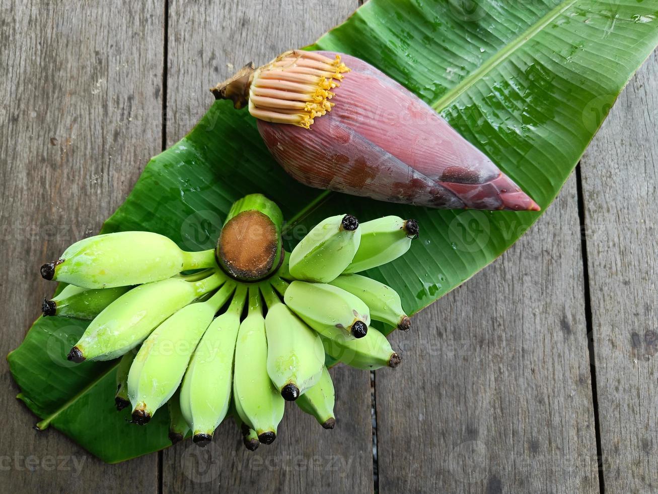 bananes vertes et fleur sur feuilles de bananier et table en bois marron photo