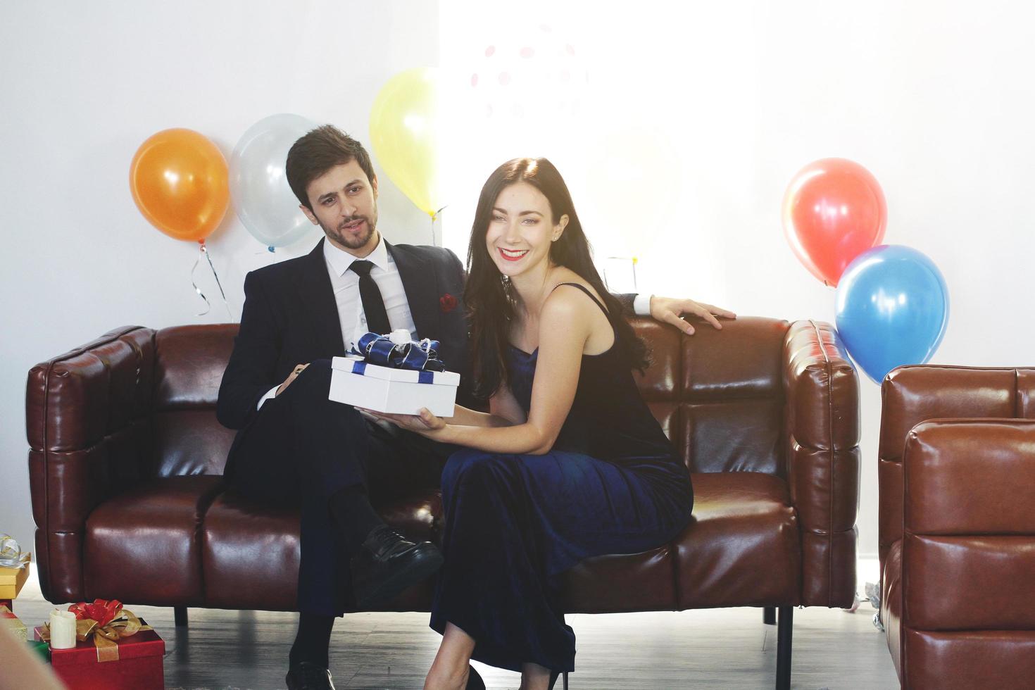 doux couple amour heureux avec petite amie boîte cadeau surprise à la fête de noël, célébration de l'anniversaire du nouvel an, décoration de la saint-valentin avec ballon coloré sur un canapé marron dans le salon photo