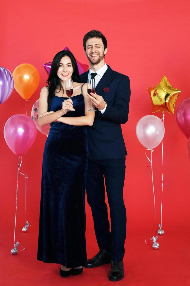 doux couple aime sourire et passer du romantique en buvant du vin à noël et en célébrant le nouvel an, la saint valentin avec un ballon coloré sur fond rouge photo