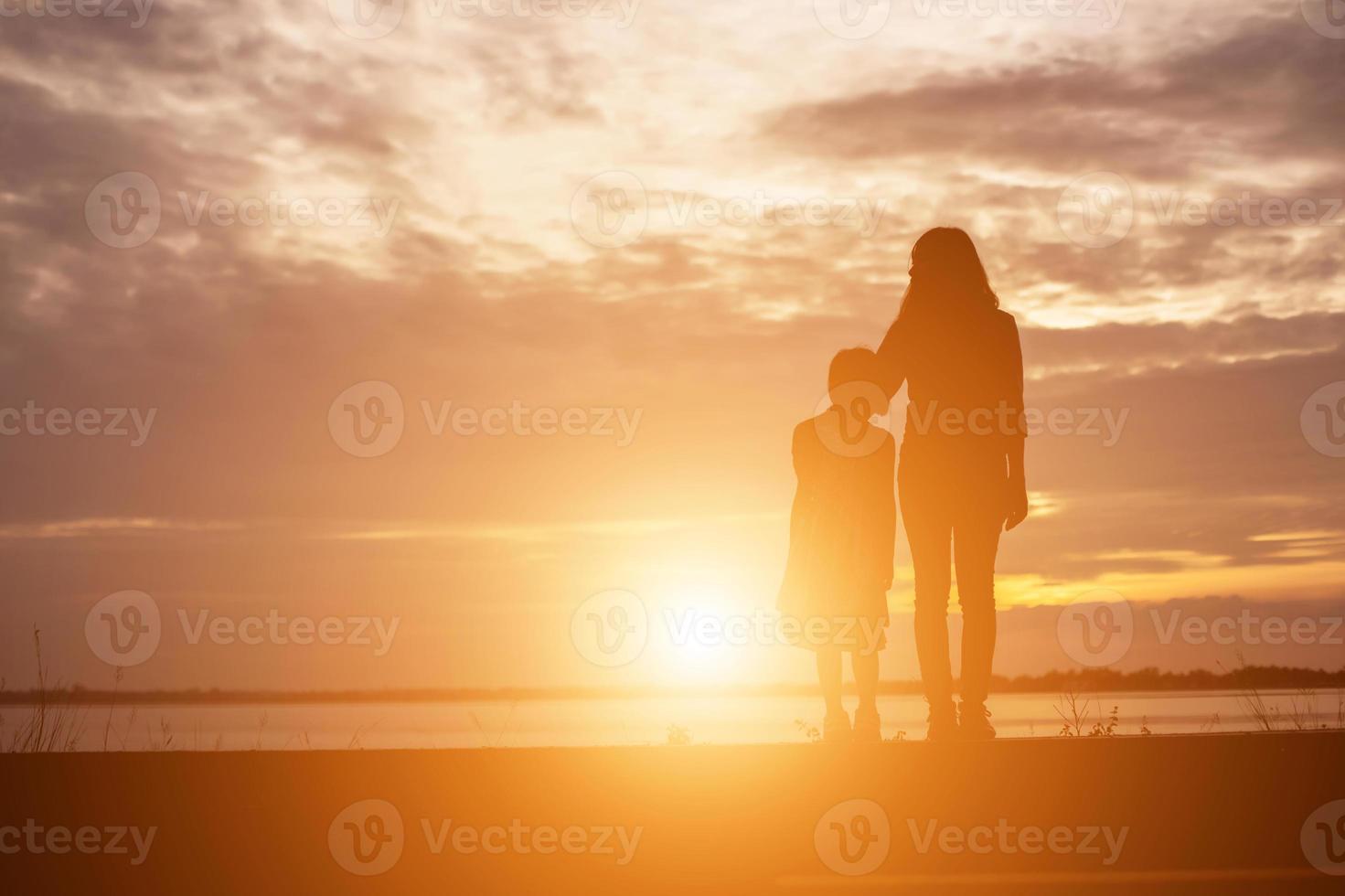 une silhouette d'une jeune fille heureuse dans les bras de sa mère aimante pour un câlin, devant le coucher de soleil dans le ciel un jour d'été. photo