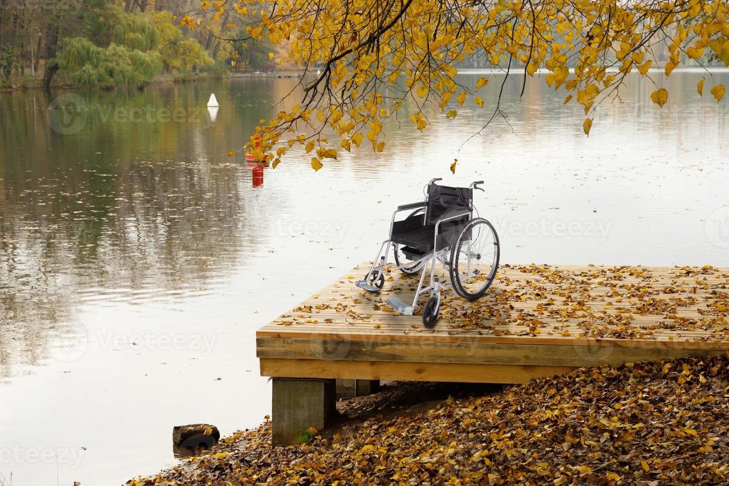 un fauteuil roulant vide sur un pont en bois près de la rivière dans le parc d'automne. le concept d'accessibilité des personnes handicapées. photo