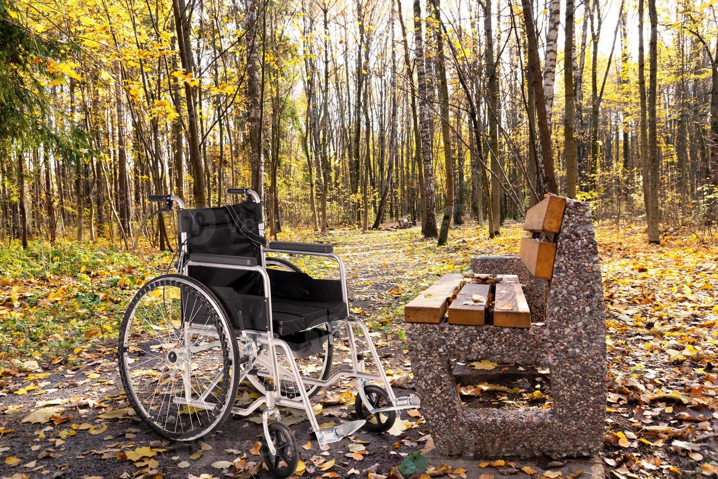 un fauteuil roulant vide garé dans un parc d'automne à côté d'un banc. le concept d'accessibilité des personnes handicapées. photo