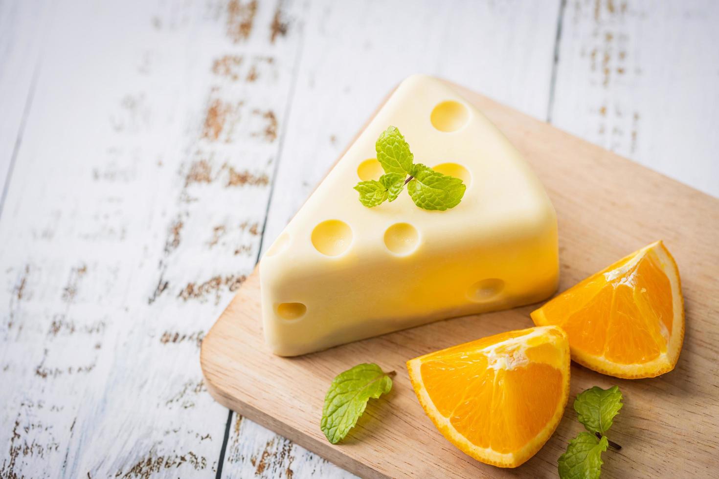 maison de gâteau au chocolat blanc frais dans une tranche de putt en forme de fromage sur une table en bois blanc et menthe, orange. concept de nourriture sucrée et de dessert. bonbons décorés pour les vacances. vue rapprochée des desserts. photo