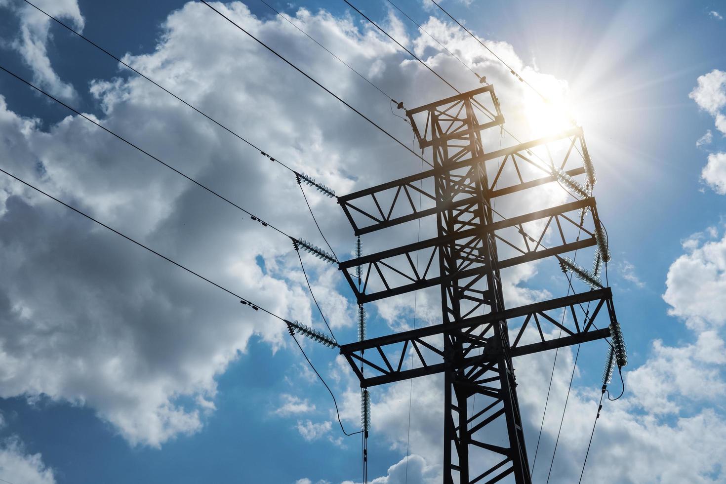 tour d'angle de transmission électrique haute tension sur fond de ciel nuageux avec rayons de soleil. photo