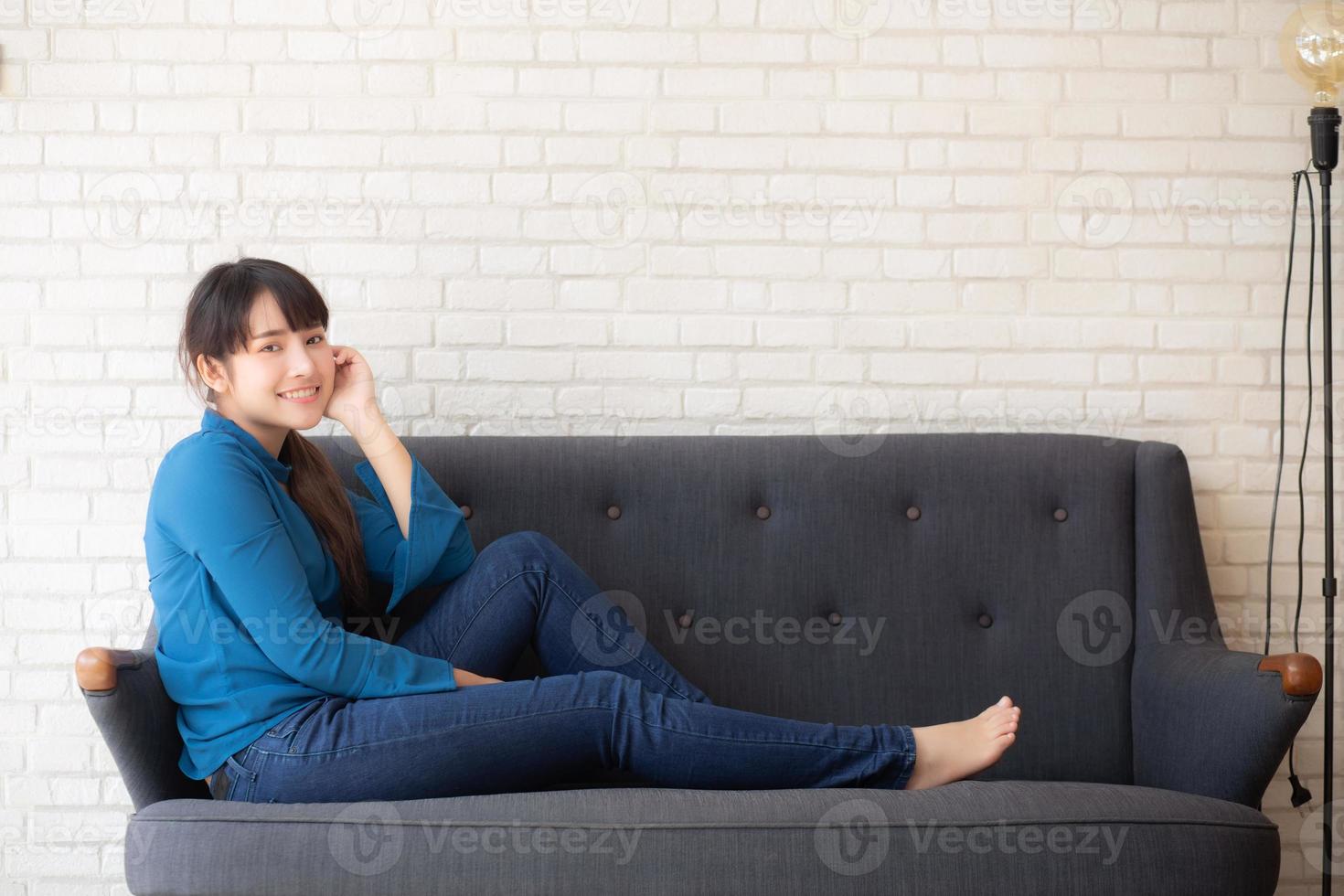 beau portrait jeune femme asiatique assise et souriante heureuse et regardant la caméra sur le canapé avec décontracté au salon, fille joyeuse et se détendre sur le canapé à la maison, concept de style de vie. photo