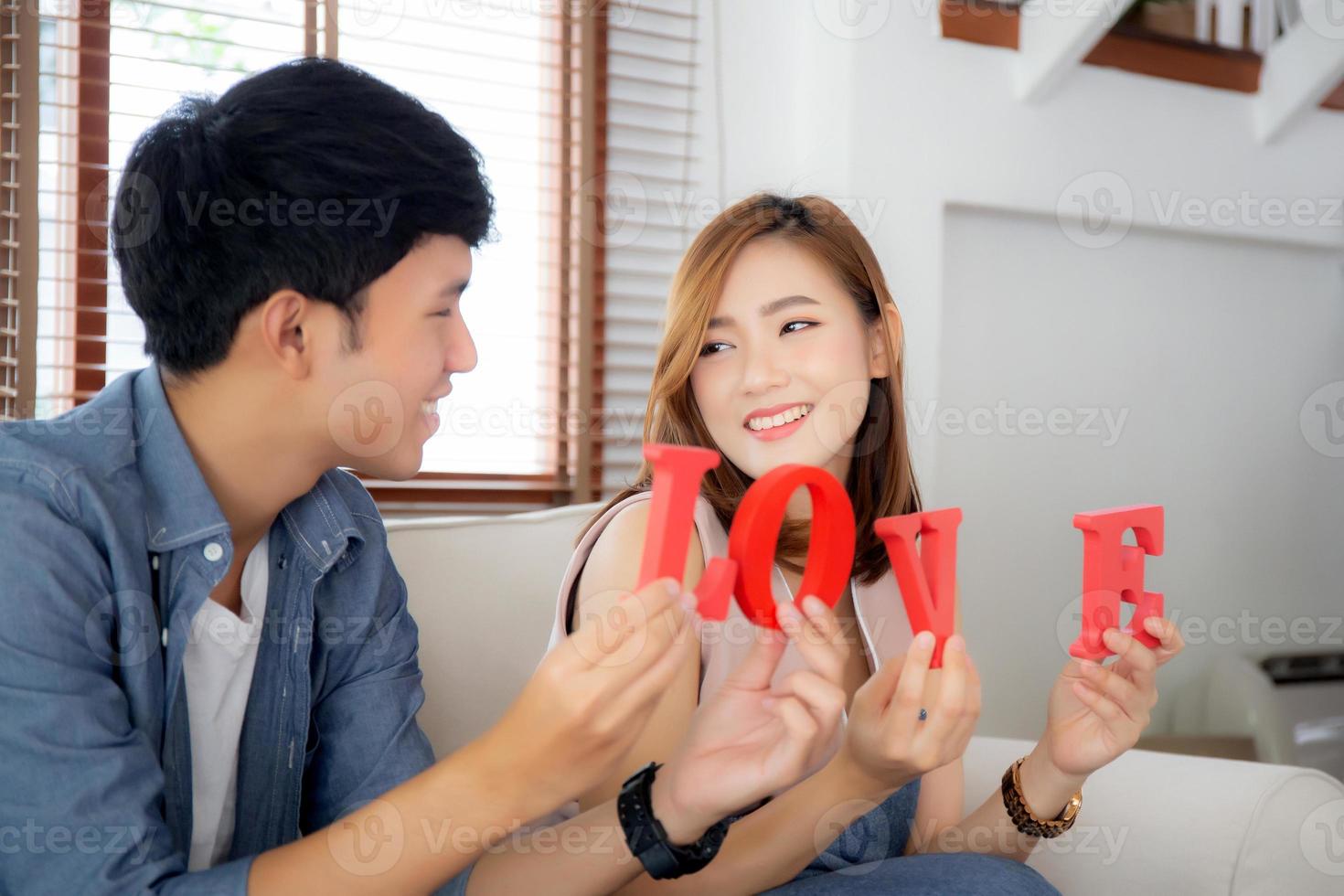 beau jeune couple asiatique assis sur un canapé tenant le mot amour ensemble dans le salon, famille mari et femme souriant avec heureux, homme et femme amoureux portant décontracté avec détente, concept de style de vie. photo