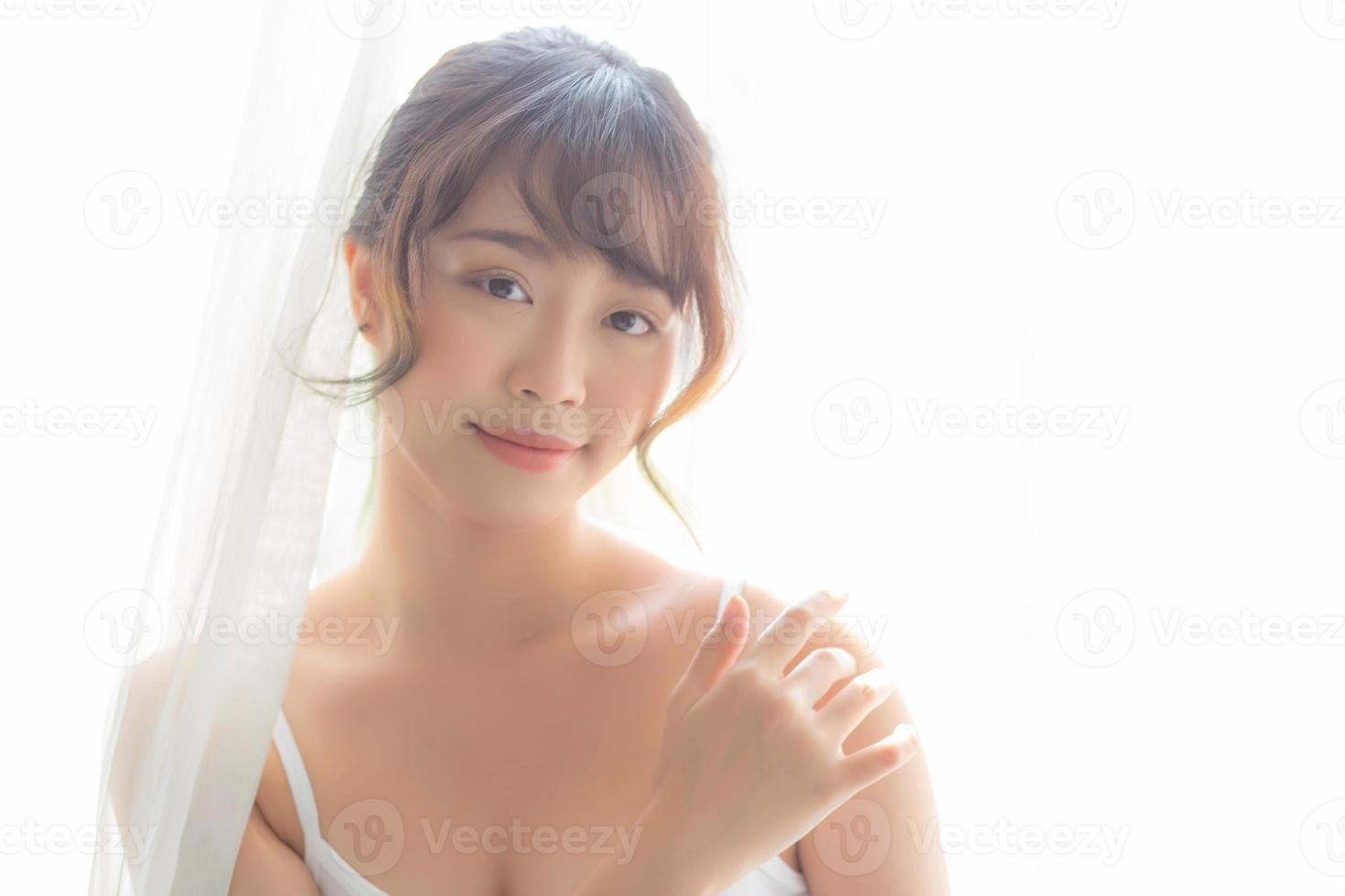 portrait de la belle jeune femme asiatique maquillage de cosmétique, main de fille toucher l'épaule et sourire attrayant, visage de beauté parfait avec bien-être dans la chambre avec concept de soins de la peau et de soins de santé. photo