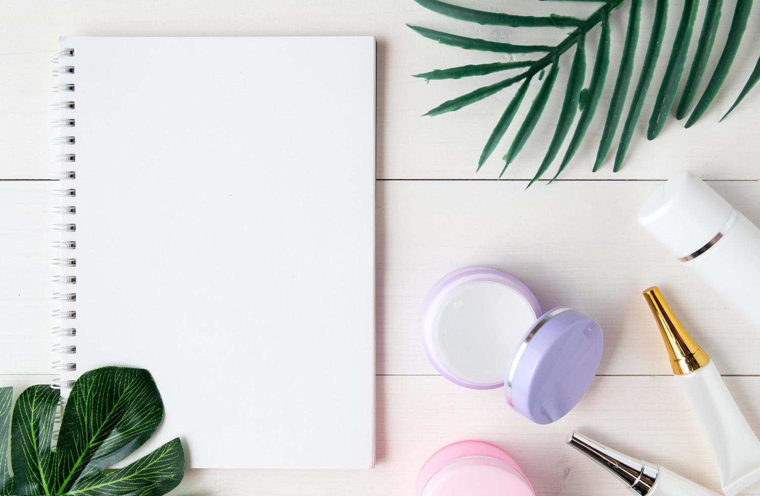 produit cosmétique et de soin de la peau et carnet et feuilles sur la table, beauté avec crème de traitement et hydratant et espace de copie du bloc-notes sur le bureau en bois, concept de santé et de bien-être, vue de dessus. photo