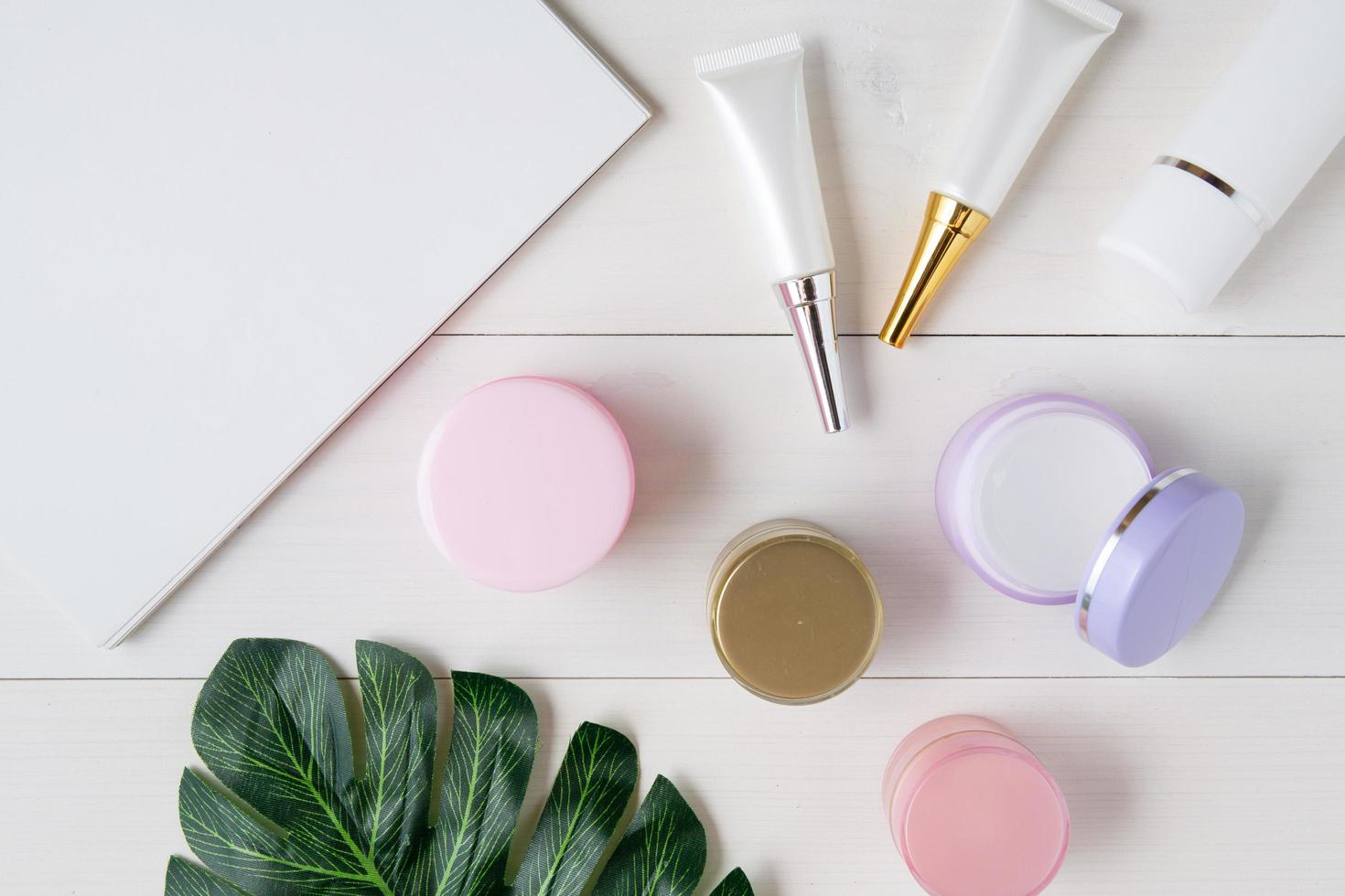 produit cosmétique et de soin de la peau et carnet et feuilles sur la table, beauté avec crème de traitement et hydratant et espace de copie du bloc-notes sur le bureau en bois, concept de santé et de bien-être, vue de dessus. photo