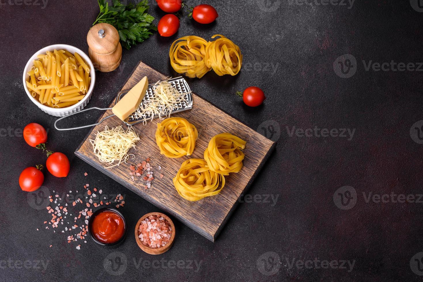 pâte de tagliatelles crues avec fromage râpé, tomates cerises, épices et herbes sur une planche à découper en bois photo