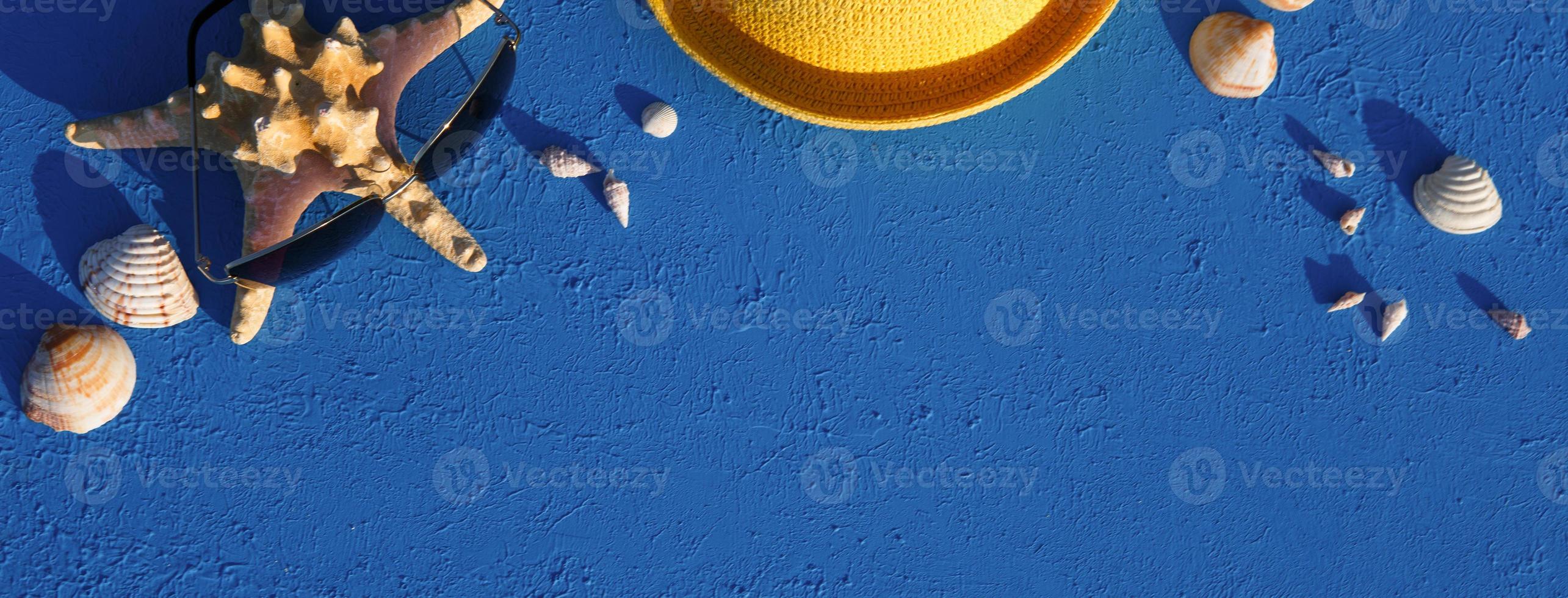 cadre avec accessoires de plage sur un thème nautique chapeau de paille jaune, lunettes de soleil, étoiles de mer et coquillages sur fond bleu. concept de vacances, voyage en mer, protection uv, natation. espace de copie. mise à plat photo