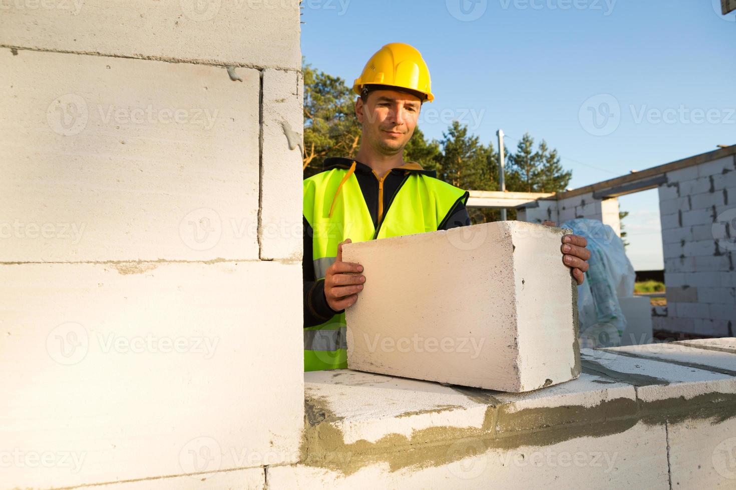 le constructeur tient entre ses mains un bloc de béton cellulaire - la maçonnerie des murs de la maison. travailleurs de la construction portant des vêtements de protection - un casque et un gilet réfléchissant. photo