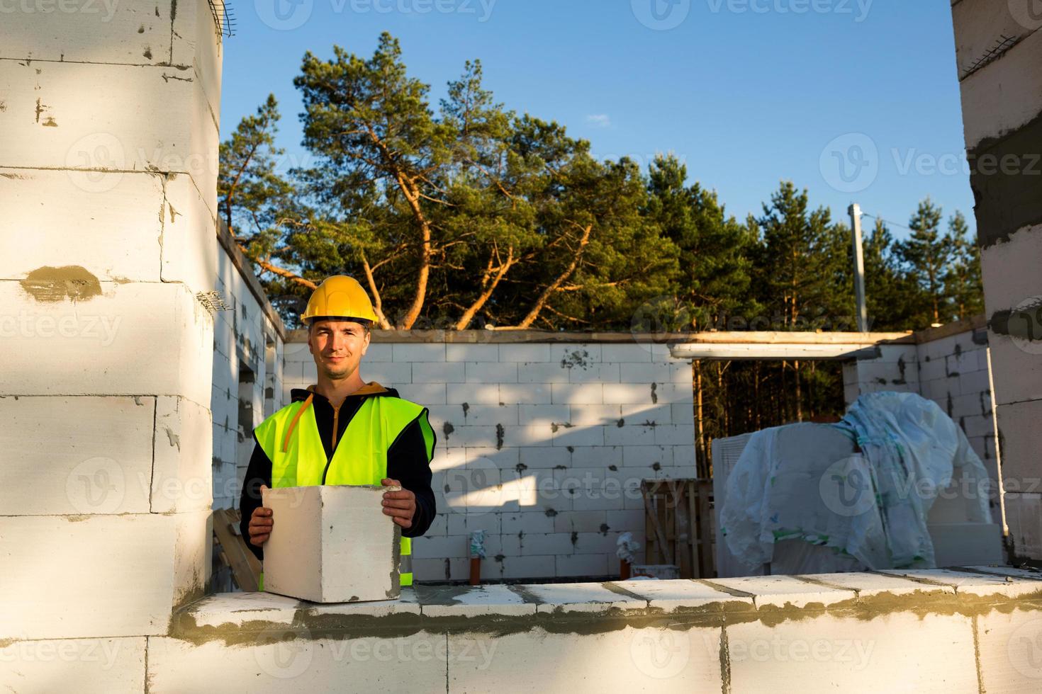 le constructeur tient entre ses mains un bloc de béton cellulaire - la maçonnerie des murs de la maison. travailleurs de la construction portant des vêtements de protection - un casque et un gilet réfléchissant. photo