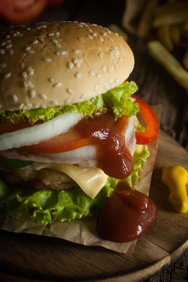 le hamburger de porc fait maison avec du bacon grillé contient des légumes, du fromage, de la laitue, de l'oignon, du piment, des épices dans un plat en bois sur un plancher en bois. photo