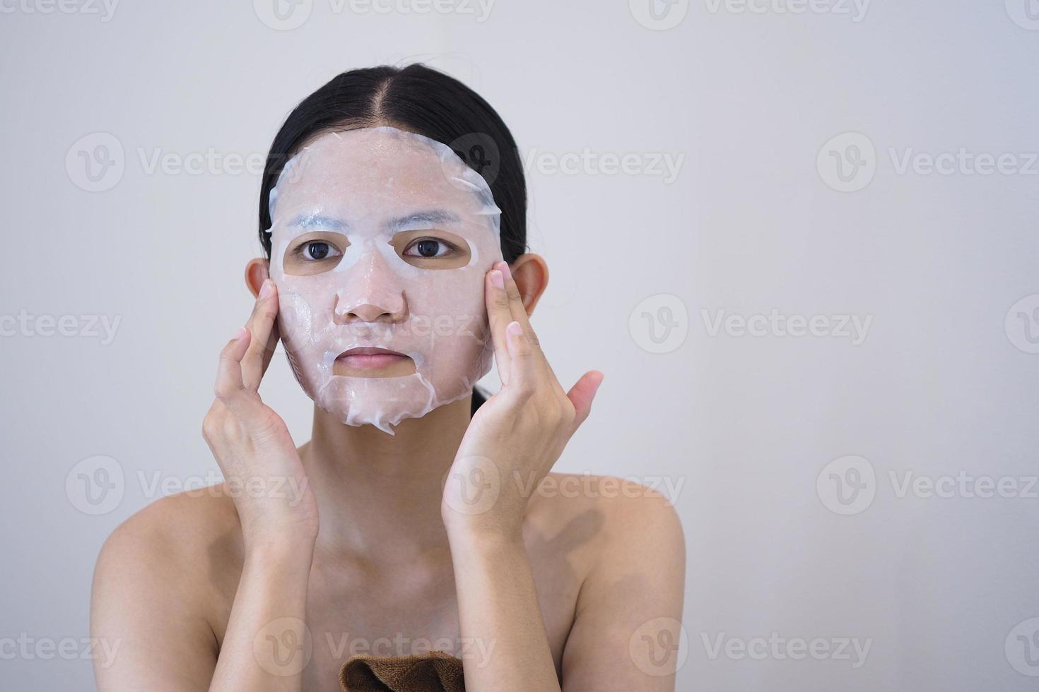 belle femme asiatique utilise un masque en feuille sur son visage. photo