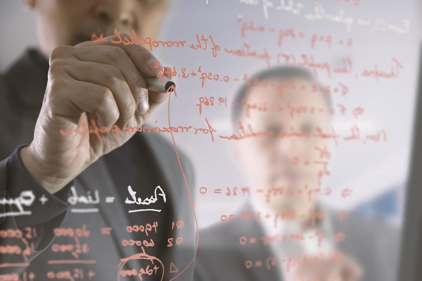 hommes d'affaires asiatiques écrivant des équations financières sur le mur de verre d'une salle de réunion tout en discutant de son collègue photo