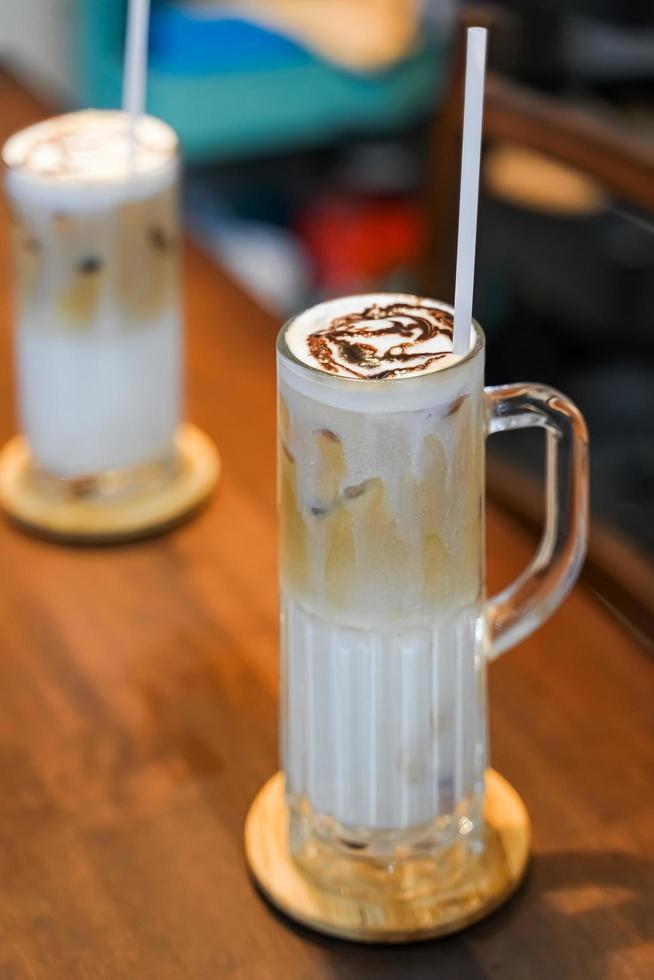 boissons ou boissons d'été rafraîchissantes, se compose de trois couches, lait froid, café et mousse de lait froide dans un grand verre, sur napperon tissé, napperon gris, table en bois brun foncé. photo