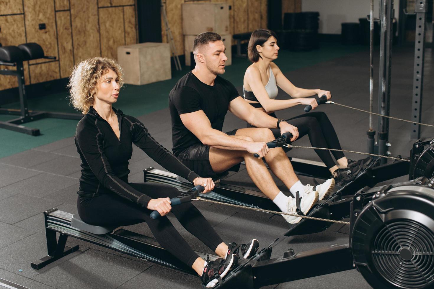 jeune homme et belles femmes travaillant avec un rameur au gymnase crossfit. photo