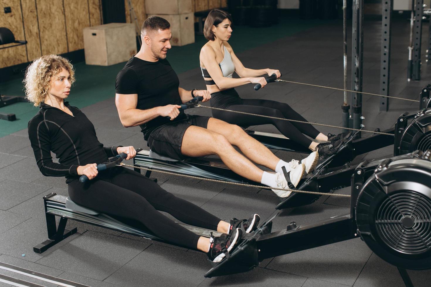 jeune homme et belles femmes travaillant avec un rameur au gymnase crossfit. photo