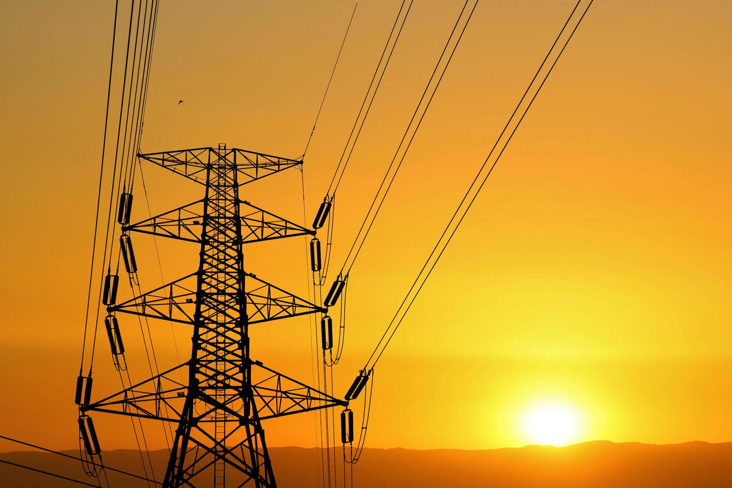 silhouette de poteaux haute tension avec fils électriques. silhouette de câbles de lignes électriques à haute tension dans un coucher de soleil orange. structure en acier des poteaux électriques. concept de transmission d'énergie électrique photo