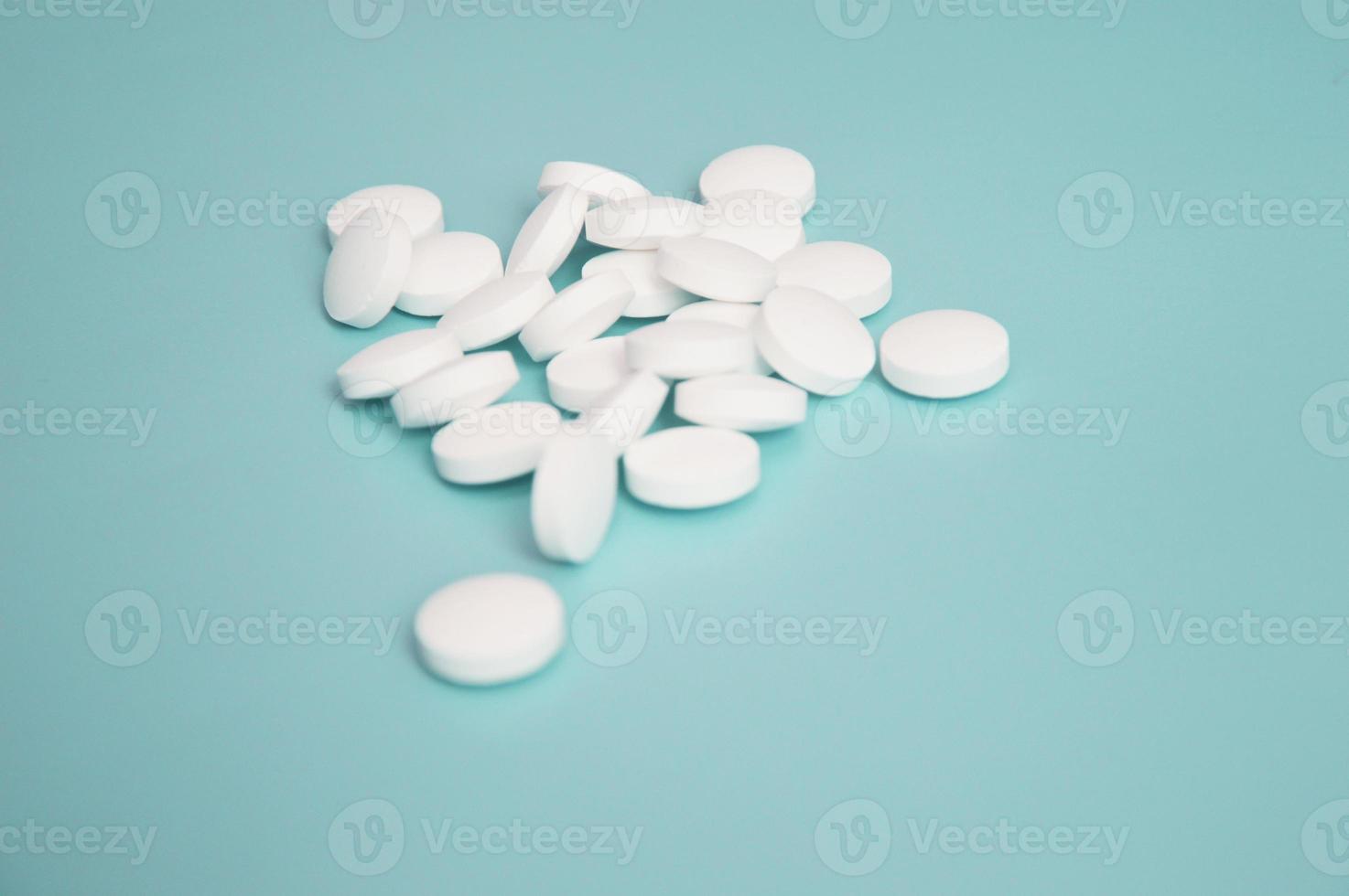 des pilules médicales blanches en vrac se trouvent sur un fond turquoise clair. santé. médicaments, bioadditifs. pharmacie, ordonnance. industrie pharmaceutique. photo