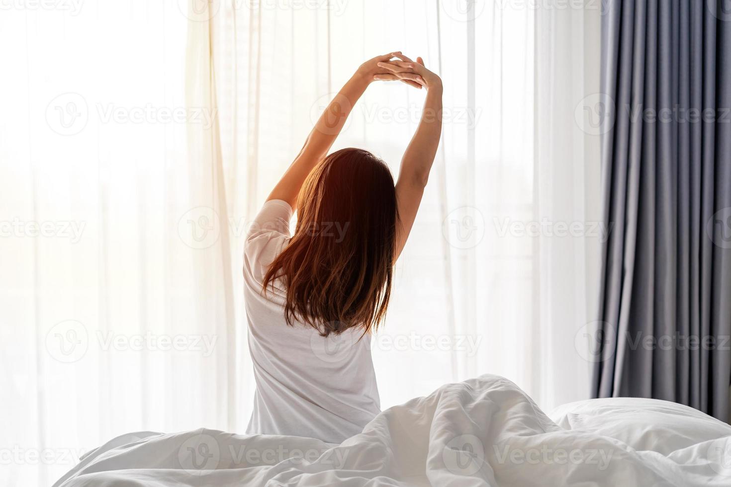 jeune femme asiatique assise sur le lit et s'étirer le matin à la maison photo