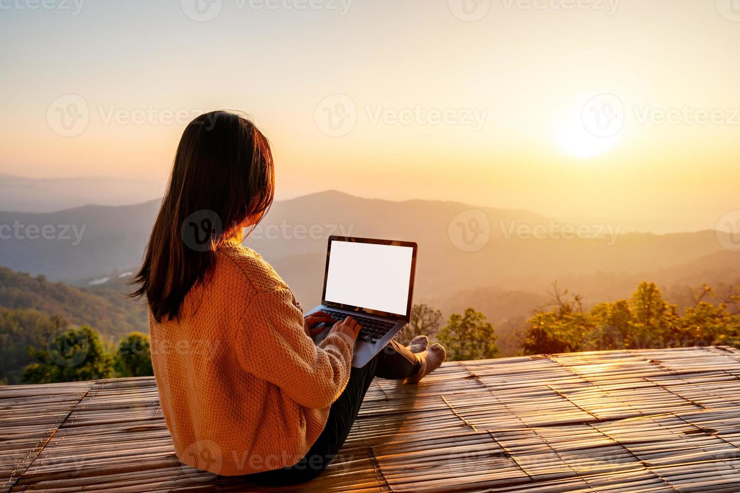 jeune femme voyageuse indépendante travaillant en ligne à l'aide d'un ordinateur portable et profitant du magnifique paysage naturel avec vue sur la montagne au lever du soleil photo