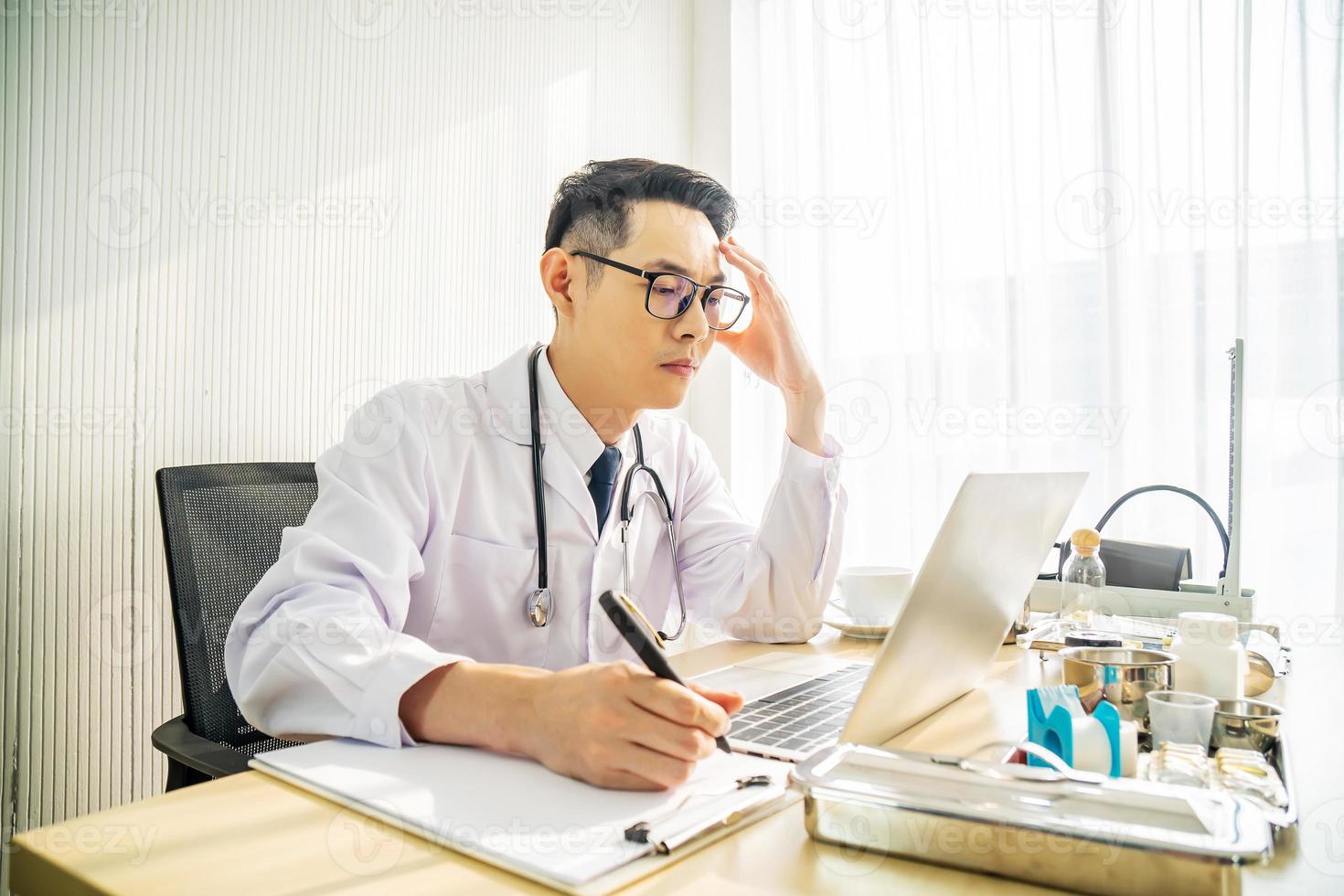 médecin asiatique troublé travaillant sur ordinateur au bureau dans une clinique hospitalière, inquiet, réfléchissant fort, concept de soins de santé pour covid19. photo