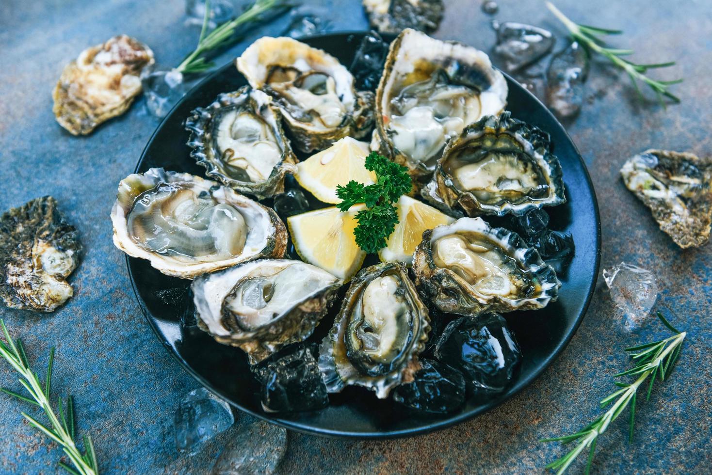 huîtres fraîches fruits de mer sur fond de plaque noire - coquille d'huître ouverte avec épices aux herbes citron romarin servi table et glace fruits de mer sains dîner d'huîtres crues au restaurant cuisine gastronomique photo