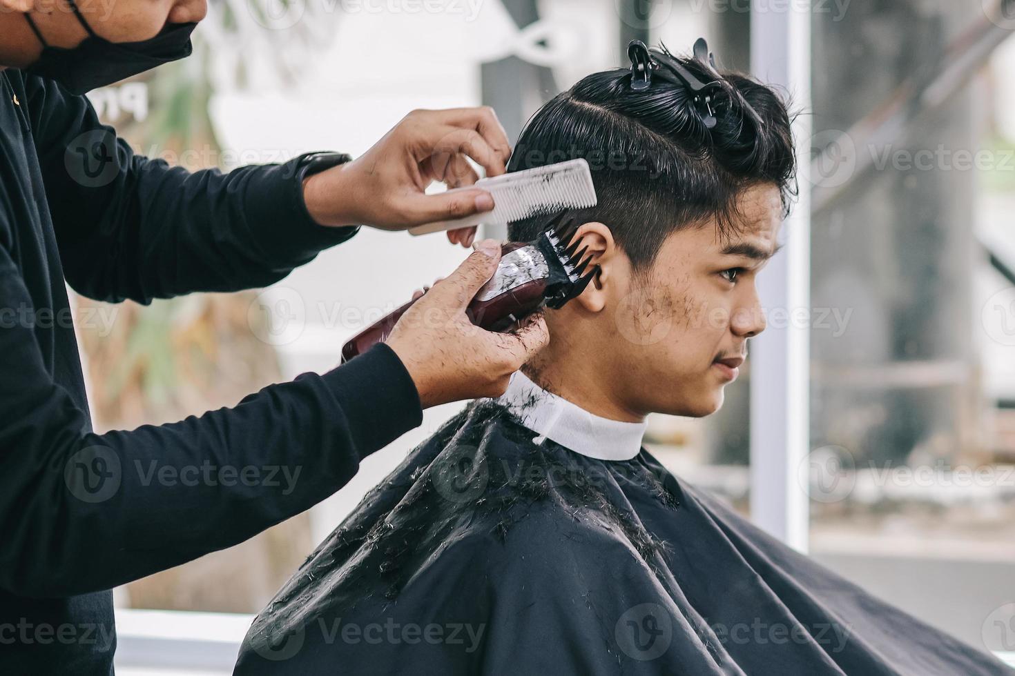 le coiffeur rase les cheveux du consommateur avec une tondeuse photo