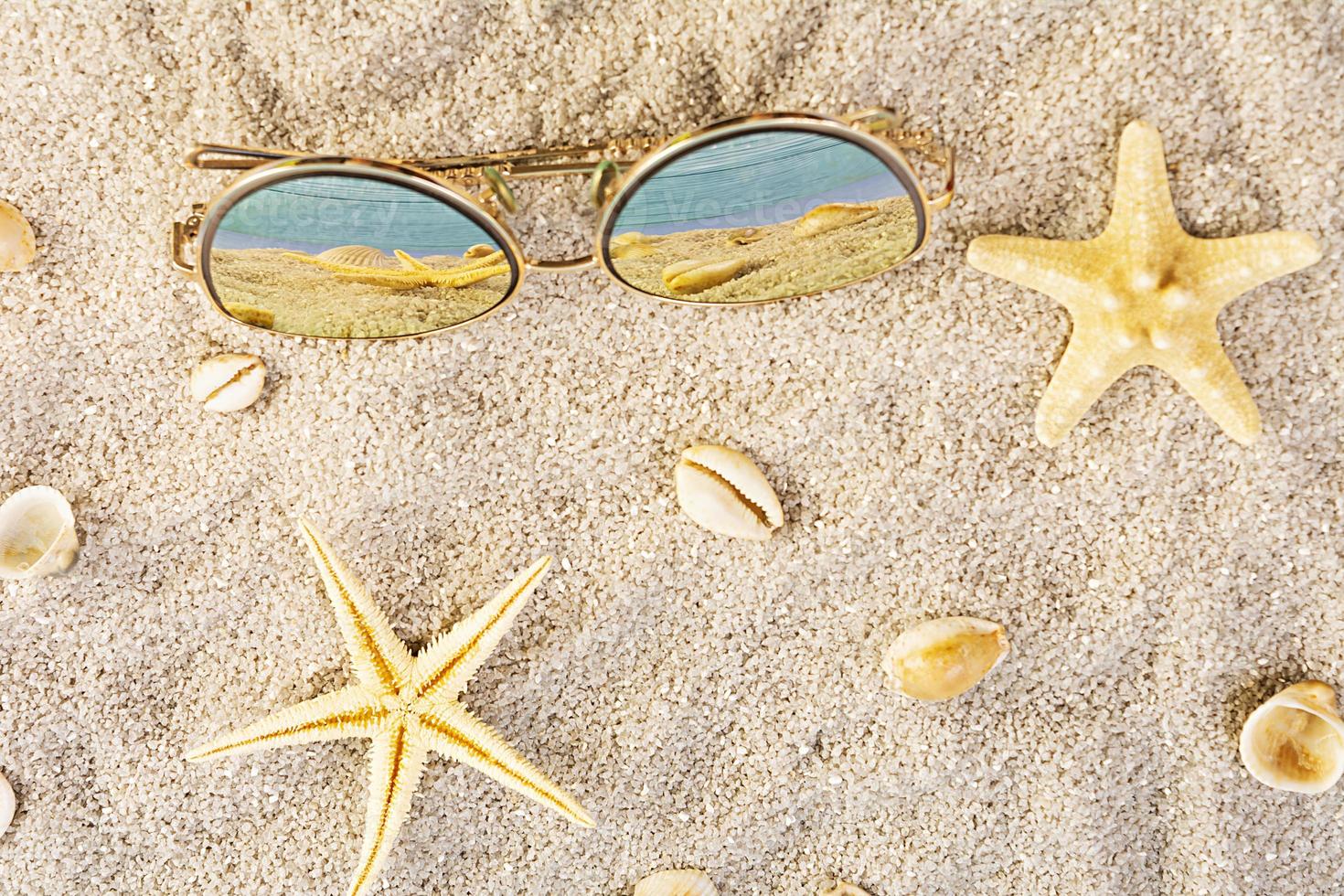 fond d'été. sable de mer avec coquillages, étoiles de mer et lunettes de soleil. notion de vacances d'été photo
