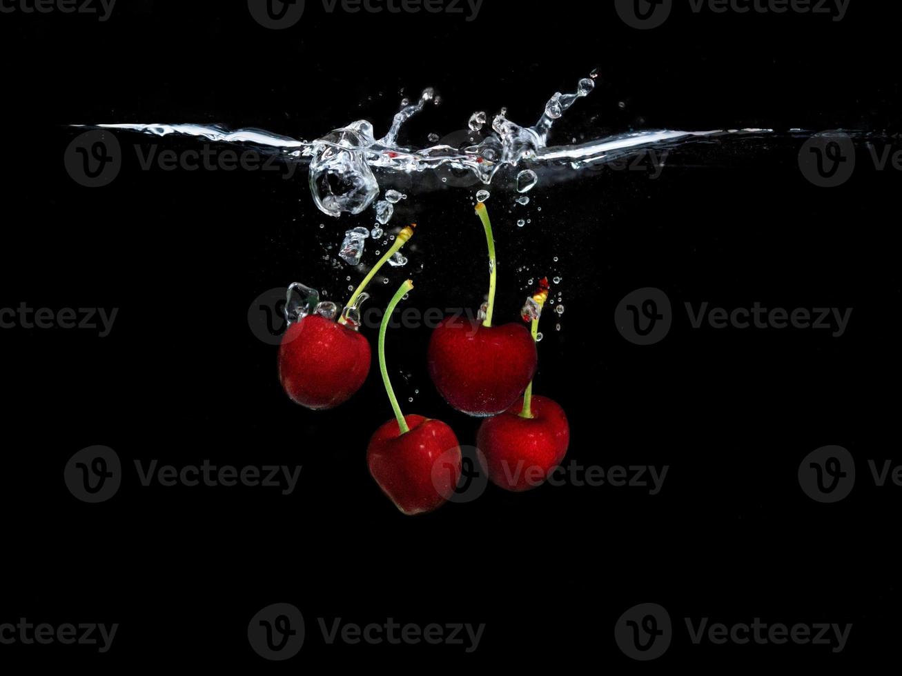 cerises douces rouges sous l'eau isolé sur fond noir photo