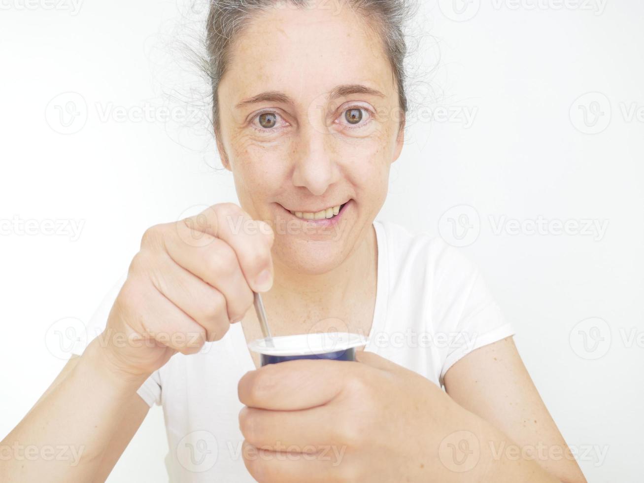 femme de quarante neuf ans dans un t-shirt blanc sur fond blanc mangeant un yaourt photo